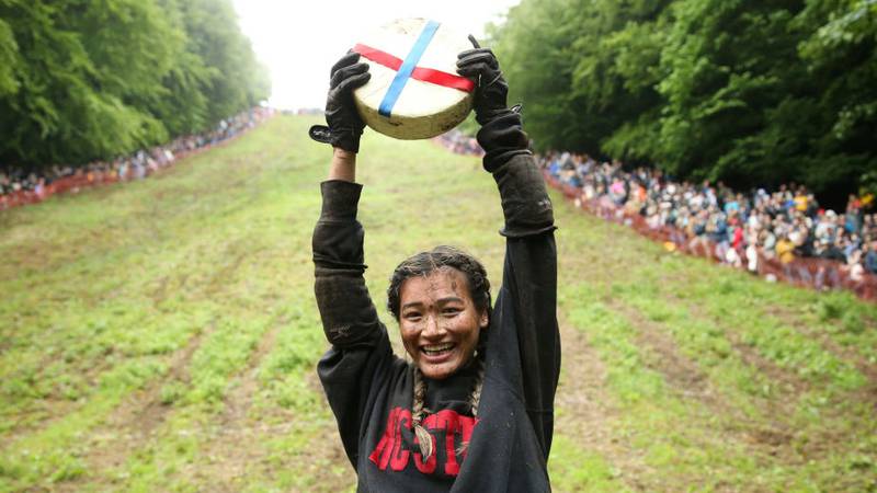GLOUCESTER, ENGLAND - JUNE 05: Abby Lampe from North Carolina celebrates her win with the cheese in the woman's race on June 05, 2022 in Gloucester, England. The Cooper's Hill Cheese-Rolling and Wake annual event returns this year after a break during the Covid pandemic. It is held on the Spring Bank Holiday at Cooper's Hill, near Gloucester and this year it happens to coincide with the Queen's Platinum Jubilee. Participants race down the 200-yard-long hill after a 3.6kg round of Double Gloucester cheese. (Photo by Cameron Smith/Getty Images)