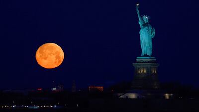 The almost full Snow Moon sets beside the Statue of Liberty before sunrise on February 8, 2020, in New York City.
